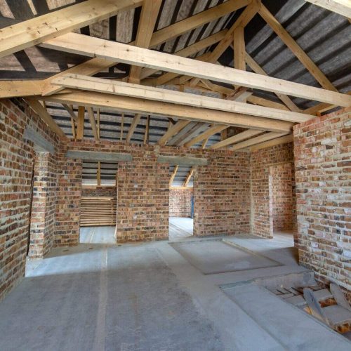Attic of a building under construction with wooden beams of a roof structure and brick walls.