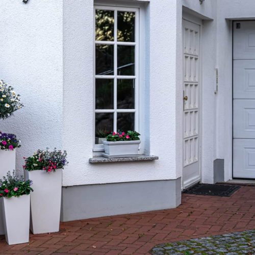 Part of the exterior of the house with white color with flowers.